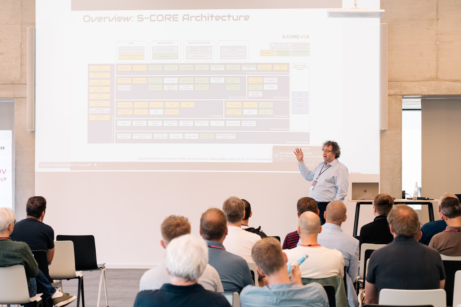 Man presenting in front of an audience, pointing at presentation slides