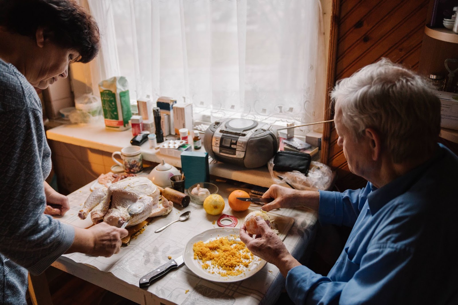 IMAGO / Addictive Stock / Hernandez and Sorokina | From the above side view of a casual male pensioner peeling orange while helping wife in preparing chicken for dinner at home.